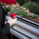 Person holding rose in front of coffin